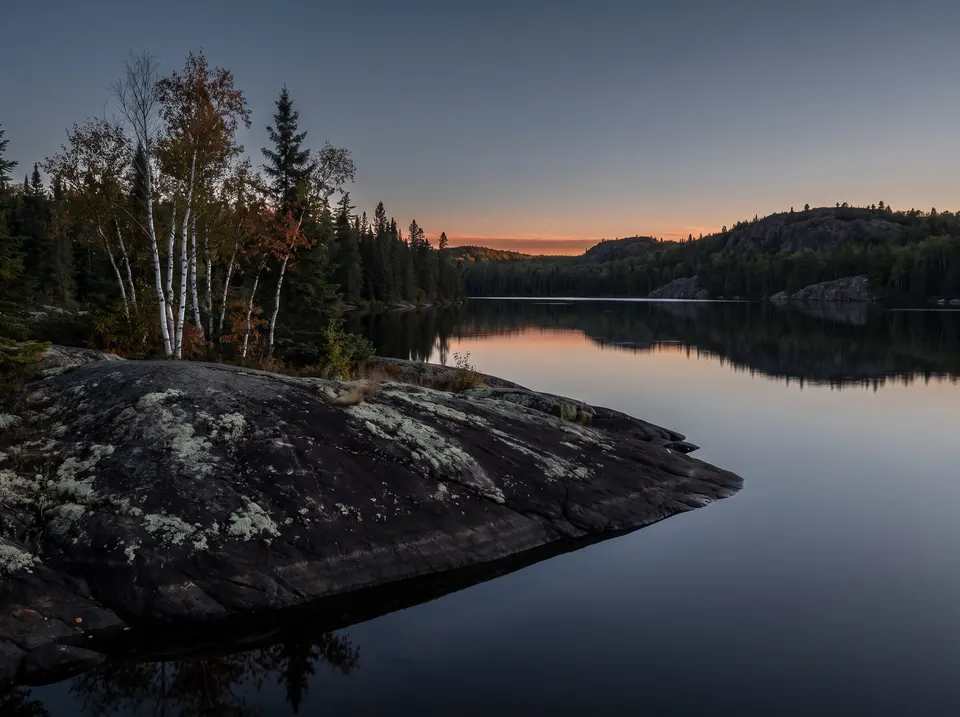 Dark rock and birches above a calm lake at dawn